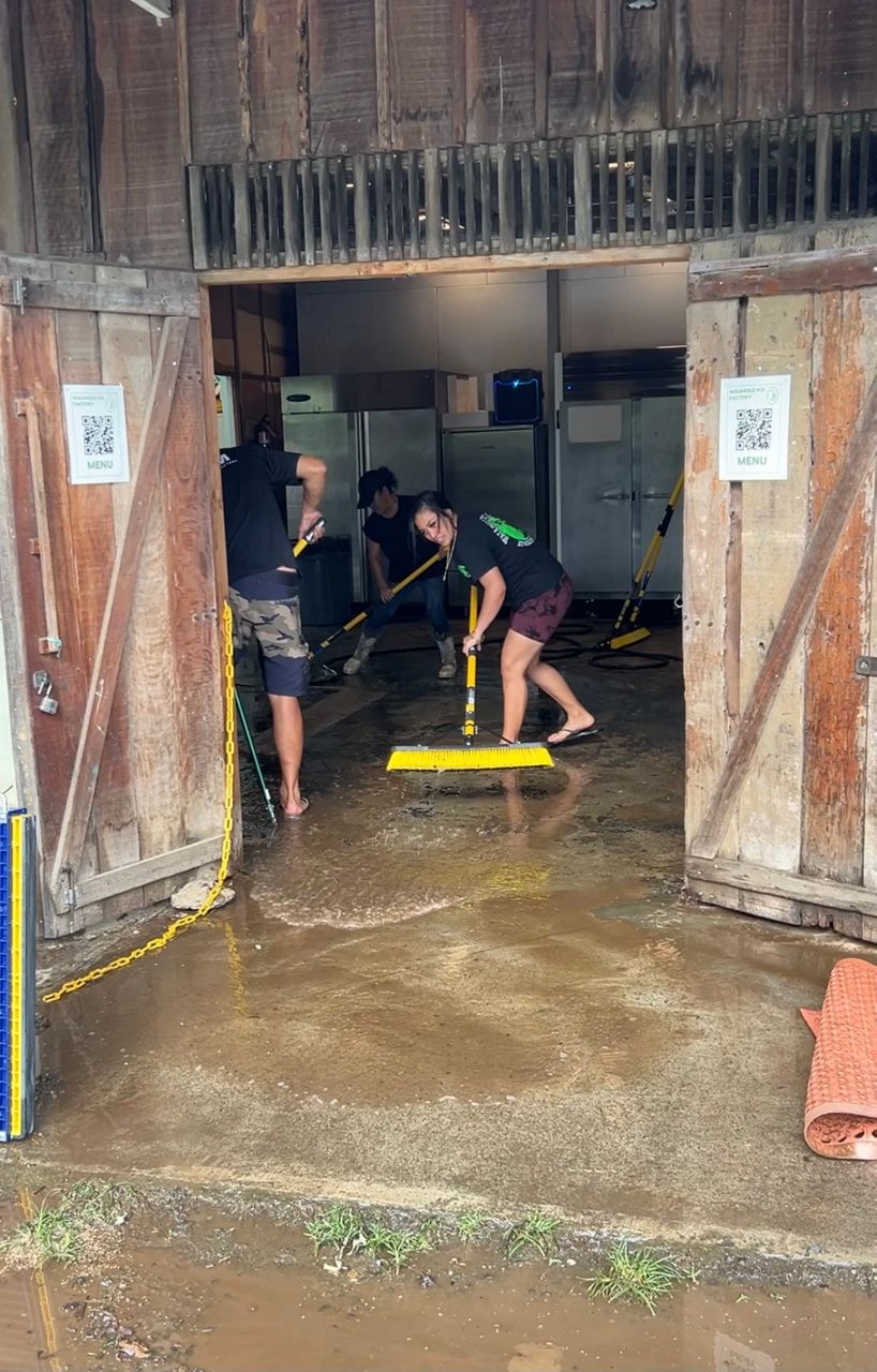 The staff at Waiahole Poi Factory sweeps the flood water out of the business a day after severe rainstorms hit the Kahaluu region. (Spectrum News/Nuy Cho)