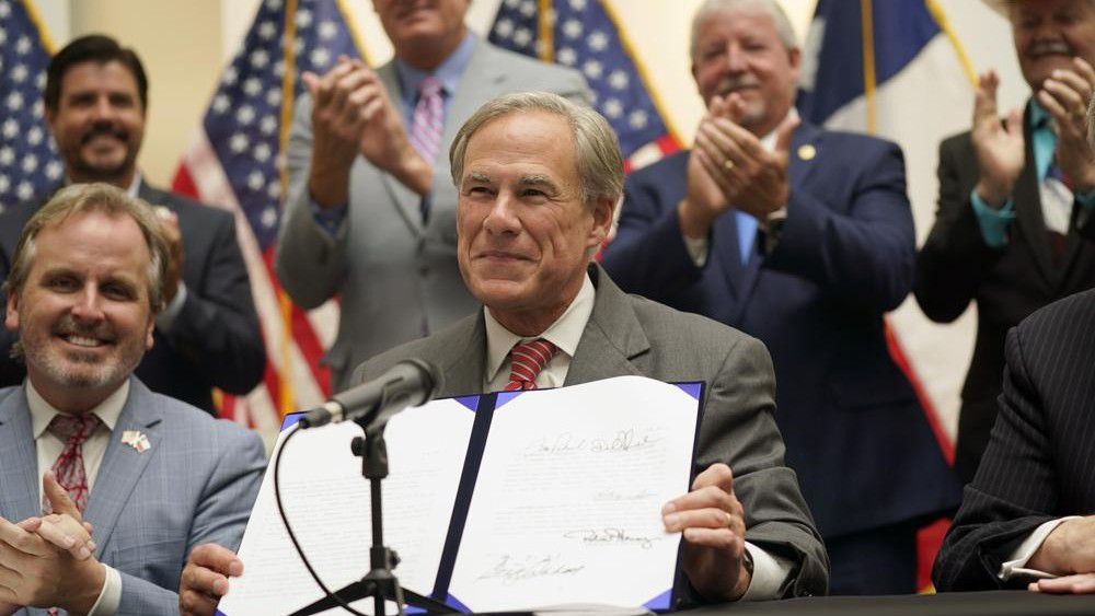 Texas Gov. Greg Abbott shows off Senate Bill 1, also known as the election integrity bill, after he signed it into law in Tyler, Texas, Tuesday, Sept. 7, 2021.  (AP Photo/LM Otero)