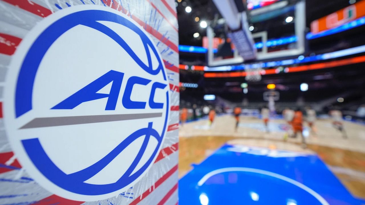 acc logo on base of basketball goal with team practicing on court in background