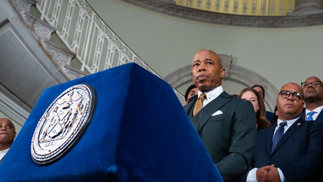 Eric Adams speaks at a blue podium in the City Hall rotunda. 