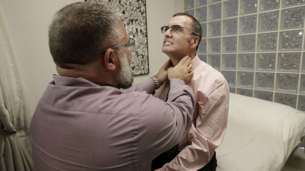 In this Jan. 26, 2018 photo, Matt Chappell, right, is checked by Dr. Christopher Schiessl during an appointment at a medical center in San Francisco. (AP Photo/Jeff Chiu)