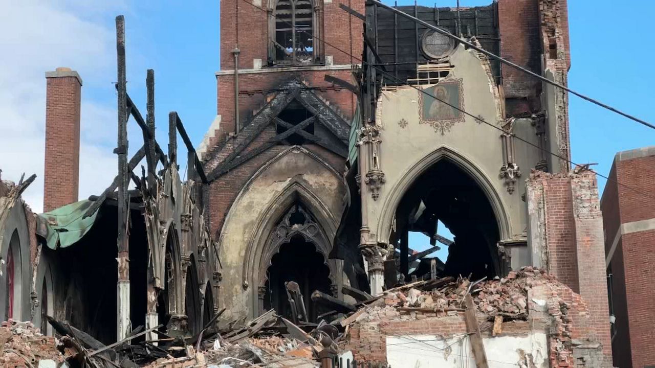 Elijah Missionary Baptist Church front, ravaged by fire, with heavy machinery on hand conducting demolition