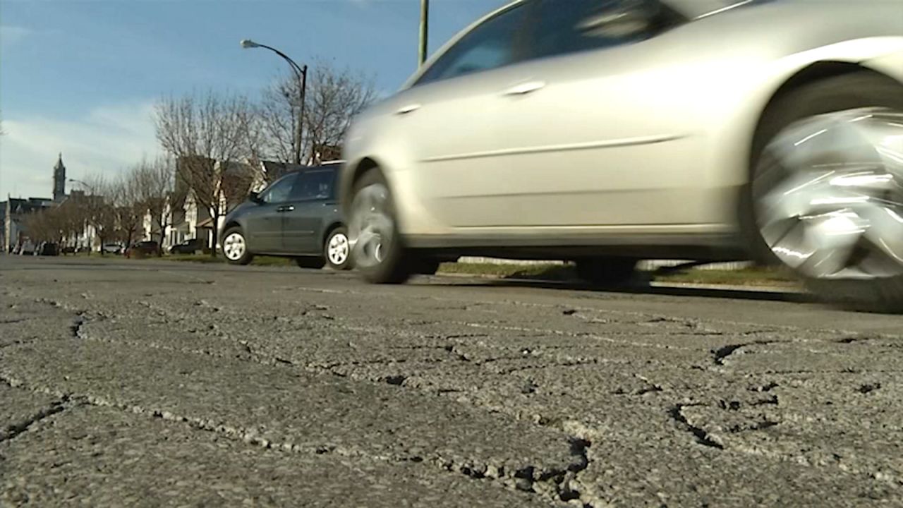 cars driving along albany road that's cracked in the foreground