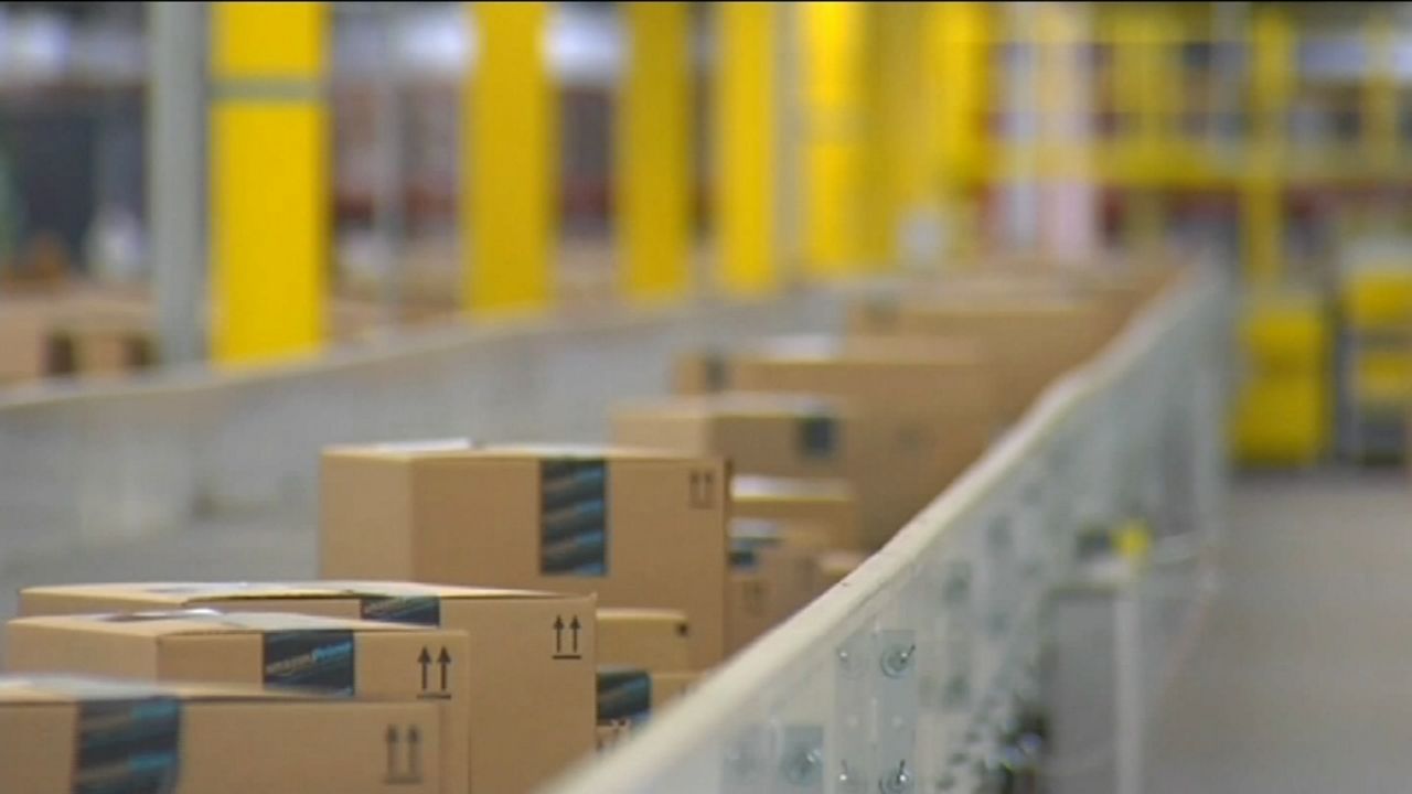 A line of brown boxes with the blue Amazon Prime sticker sit on a white assembly line. Yellow columns are in the distance.