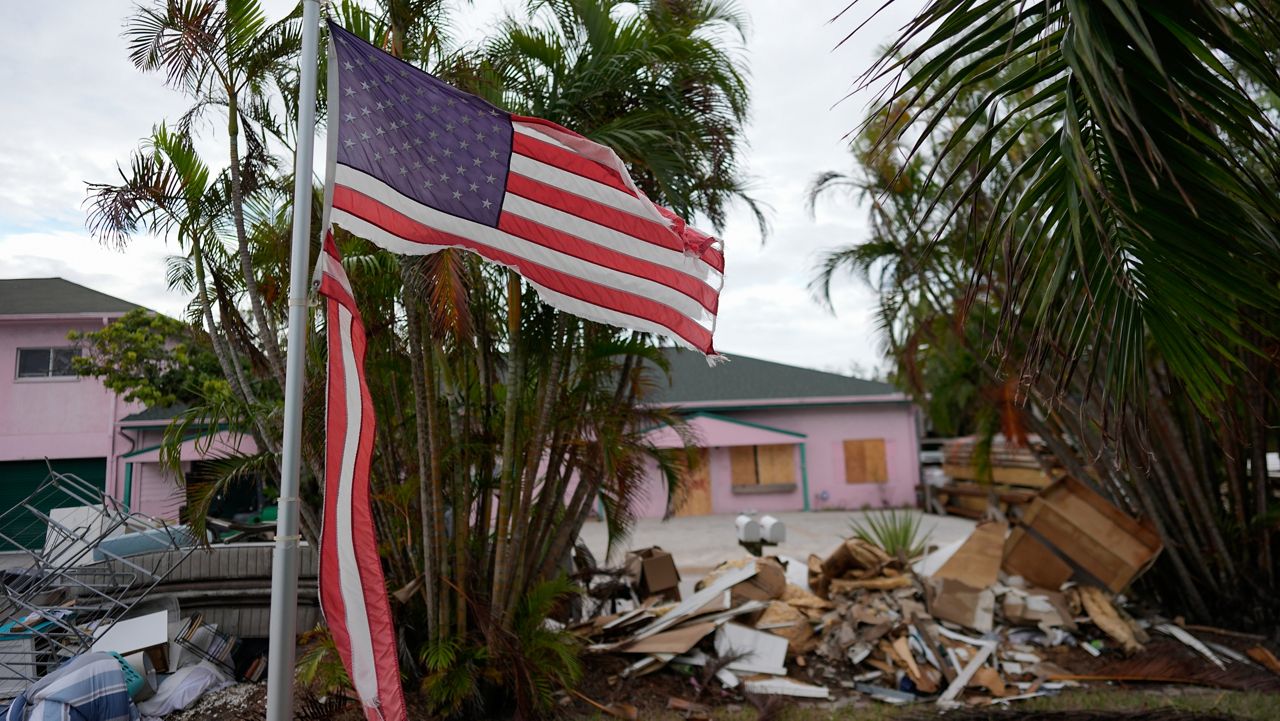 FILE - A tattered American flag flaps outside a home as furniture and household items damaged by Hurricane Helene flooding sit piled along the street awaiting pickup, ahead of the arrival of Hurricane Milton, in Holmes Beach on Anna Maria Island, Fla., Tuesday, Oct. 8, 2024. (AP Photo/Rebecca Blackwell, File)