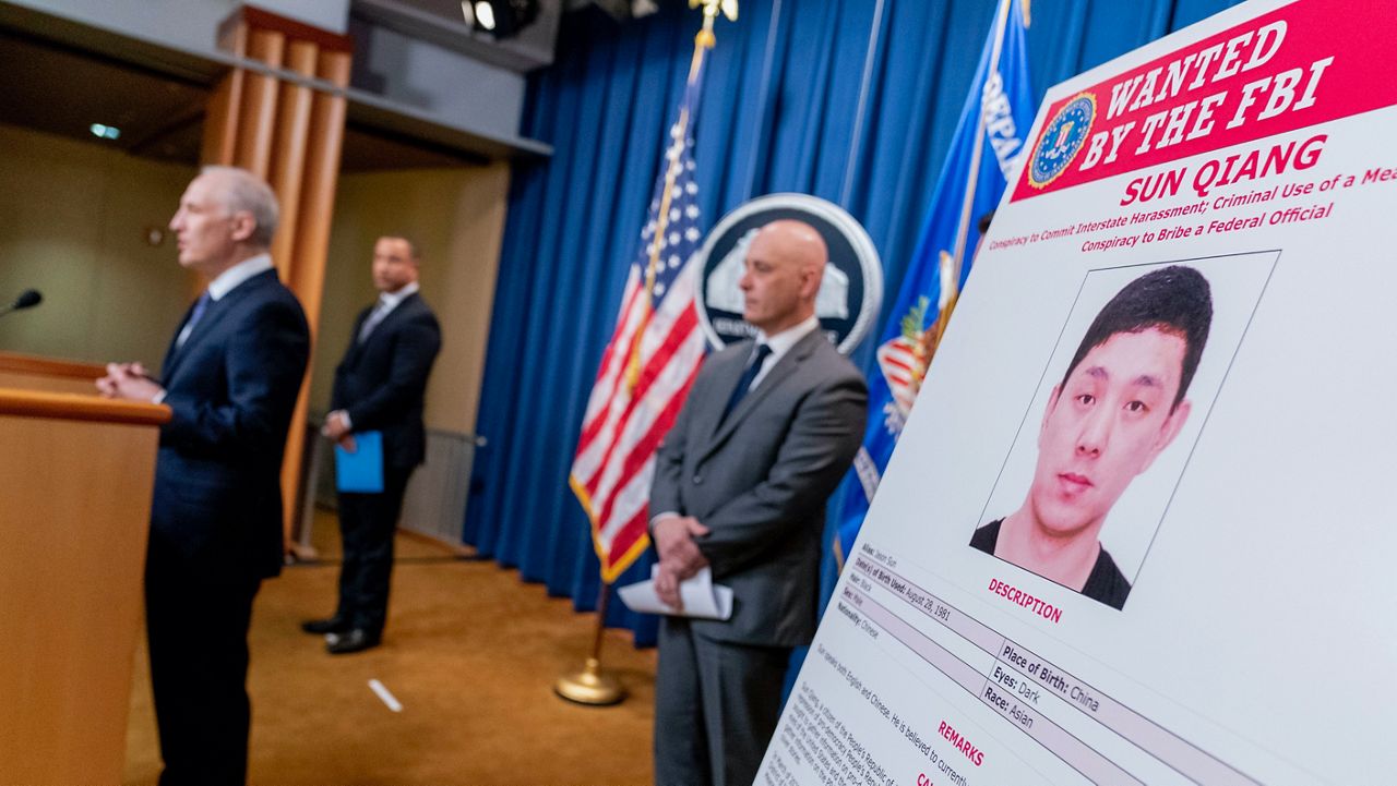 A FBI wanted poster for Sun Qiang is visible as officials speak at a news conference at the Justice Department. (AP Photo/Andrew Harnik)