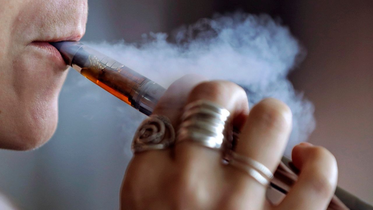 A woman using an electronic cigarette exhales a puff of smoke  