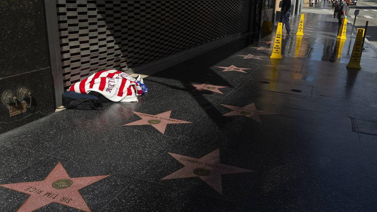 Workers clean the sidewalk of the closed Hollywood Pantages Theatre, as a homeless person sleeps under a blanket on the Hollywood Walk of Fame in Los Angeles on Tuesday, March 24, 2020. (AP Photo/Damian Dovarganes)
