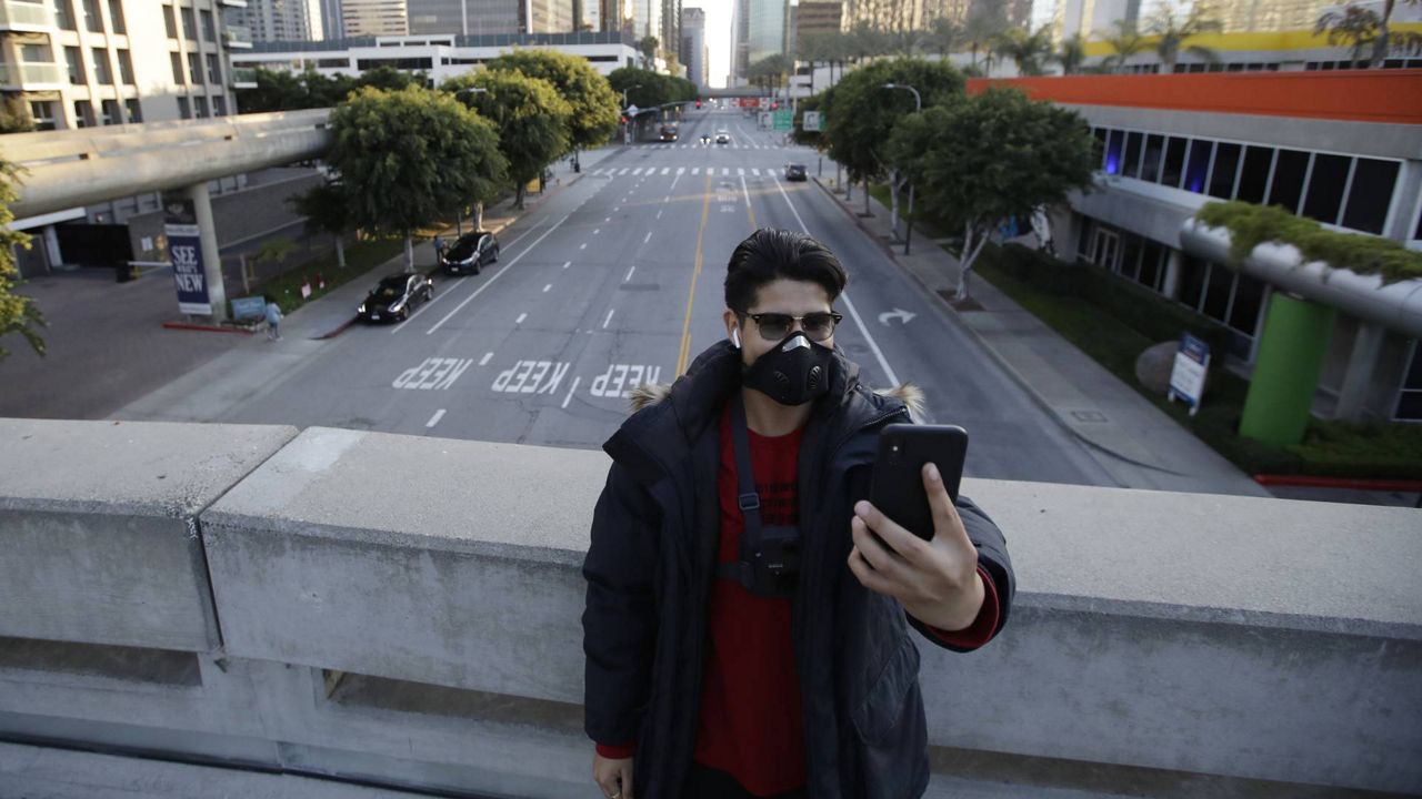 A man wears a mask as he takes a selfie in front of a near-empty downtown district on April 1, 2020, in L.A. (AP/Marcio Jose Sanchez)