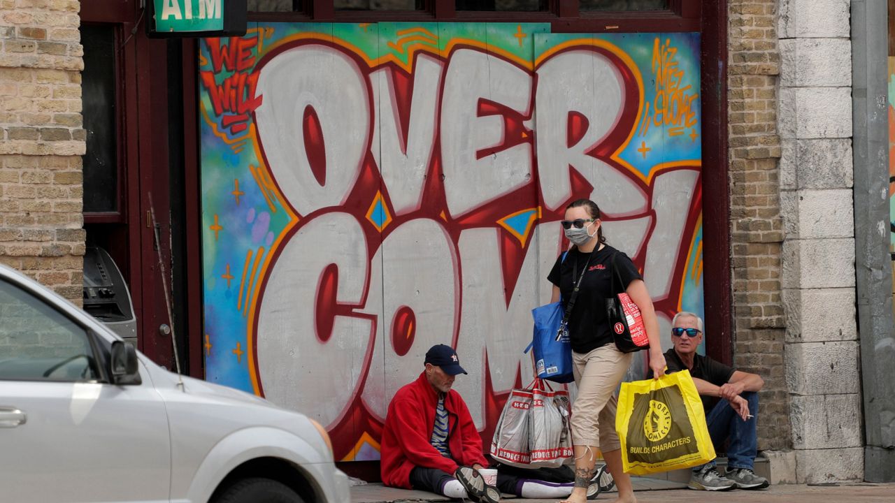 A woman wears a mask as she walks past a boarded up business in downtown Austin, Texas, Monday, April 6, 2020. (AP Photo/Eric Gay)