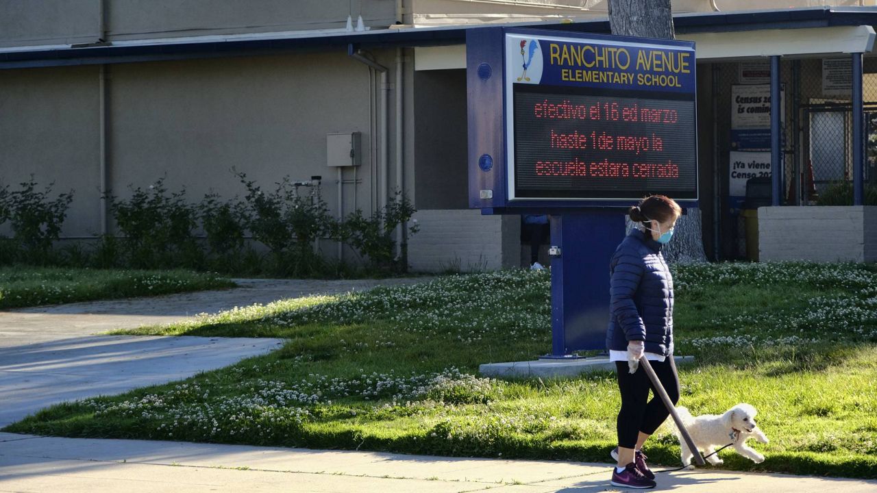 A woman wearing a protective mask for coronavirus walks her dog past a closed Ranchito Avenue Elementary School in the Panorama City section of L.A. on April 15, 2020. (AP/Richard Vogel)  