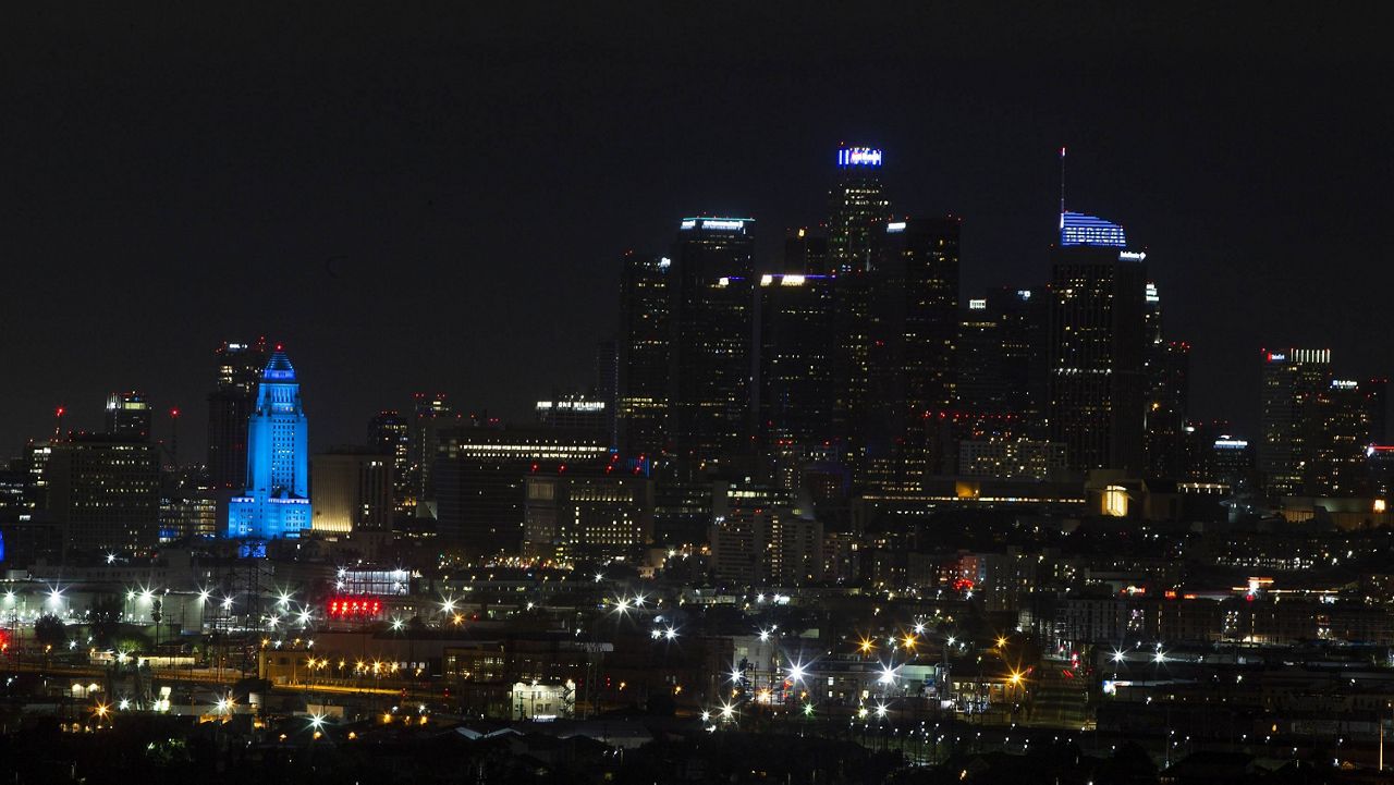 Los Angeles City Hall, bottom left, is seen lit up in blue with the Los Angeles night skyline, Saturday, April 19, 2020. (AP Photo/Damian Dovarganes)