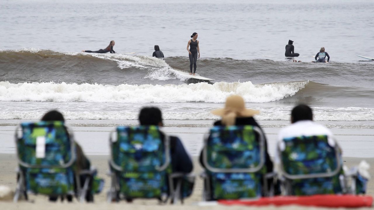 People sit on beach chairs and watch surfers Thursday, April 30, 2020, in Newport Beach, Calif. (AP Photo/Marcio Jose Sanchez)