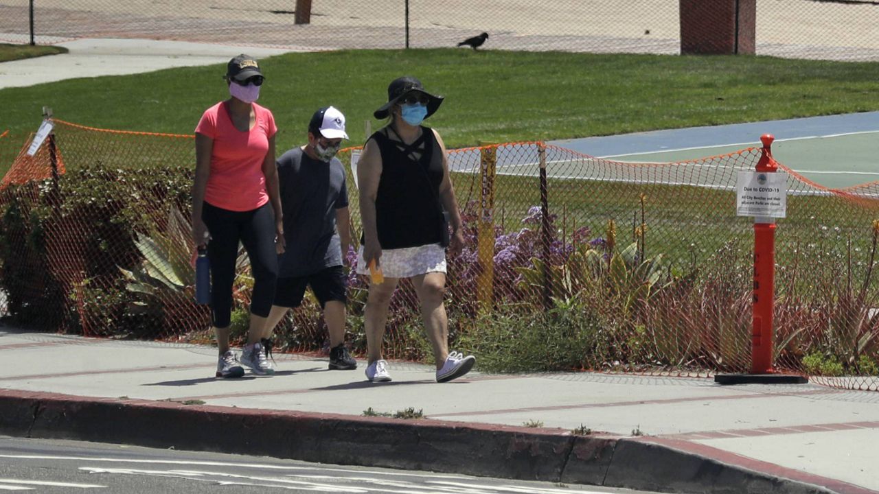 In this May 3, 2020 photo, people walk past a closed off beach, in Laguna Beach, Calif. (AP/Marcio Jose Sanchez)