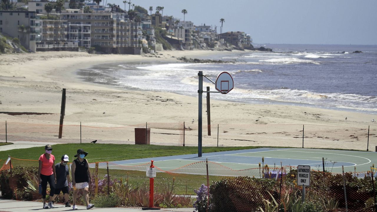In this May 3, 2020 file photo people walk past a closed off beach, in Laguna Beach, Calif. (AP Photo/Marcio Jose Sanchez,File)