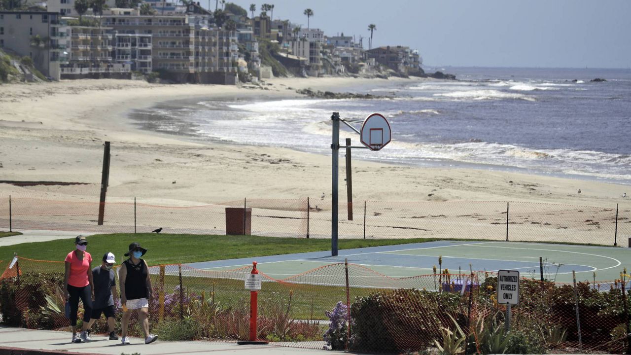 In this May 3, 2020 file photo people walk past a closed off beach, in Laguna Beach, Calif. On Monday, no new COVID-related fatalities were reported, leaving the death toll at 810. (AP Photo/Marcio Jose Sanchez)