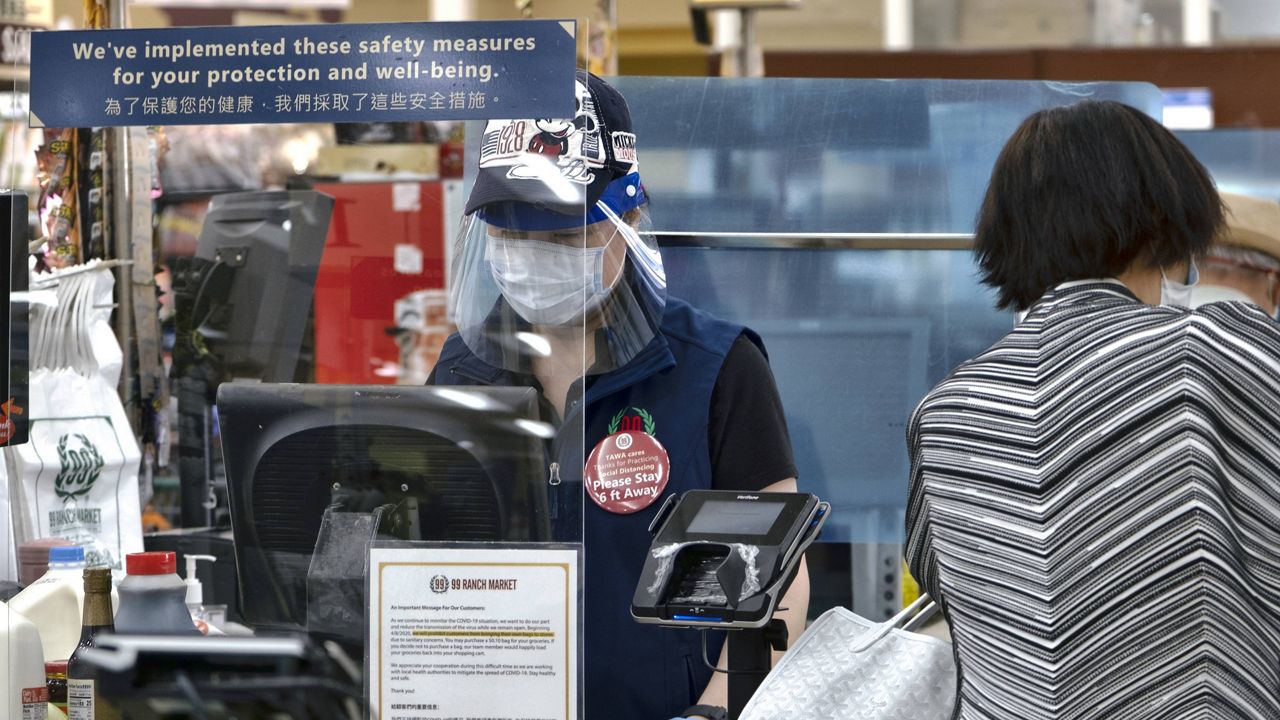 A grocery worker, wearing a face shield with protective mask and gloves, helps to check out a customer from behind a plexiglass barrier at the 99 Ranch Market in the Van Nuys section of Los Angeles on Tuesday May, 5, 2020. (AP Photo/Richard Vogel)