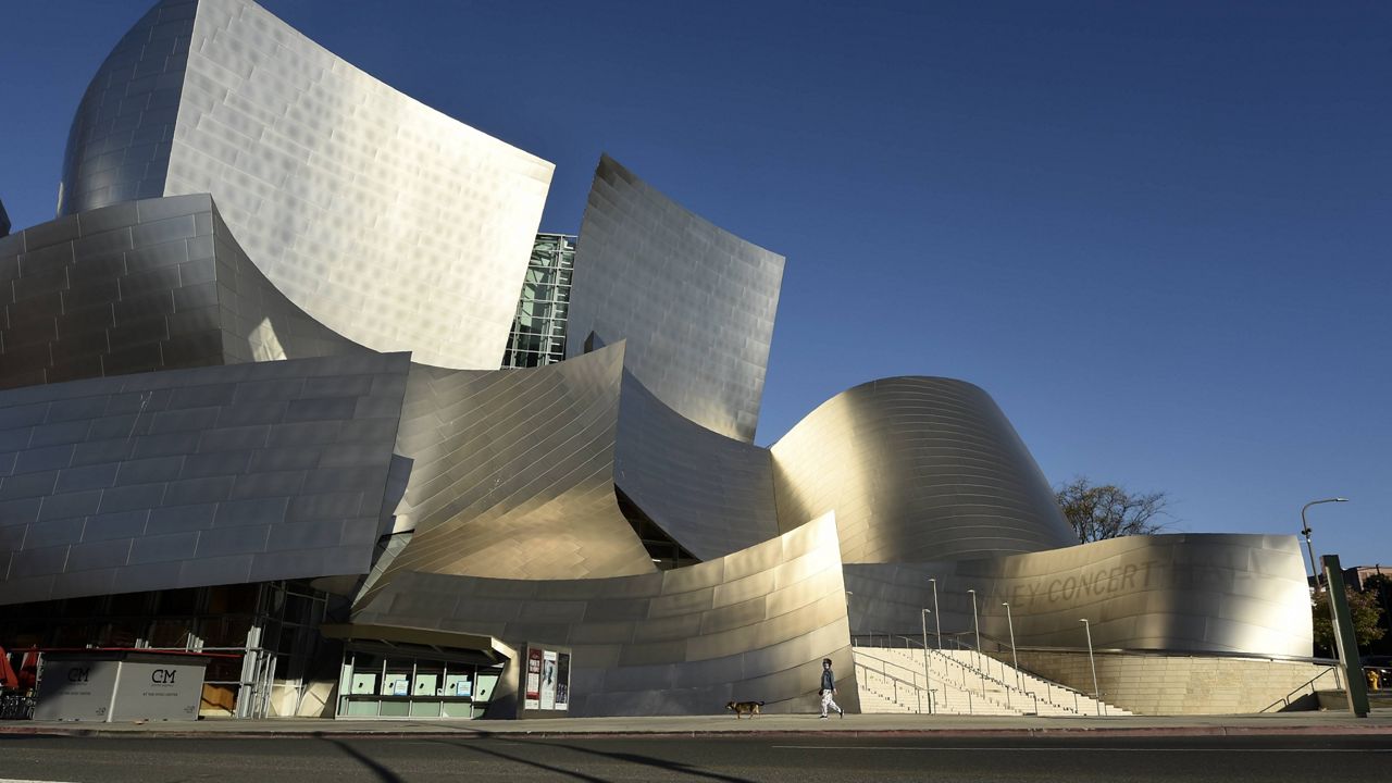 In this Saturday, April 25, 2020 photo, a woman walks her dog past the Walt Disney Concert Hall on deserted Grand Avenue as stay-at-home orders continue due to the coronavirus pandemic, in Los Angeles. (AP Photo/Chris Pizzello)