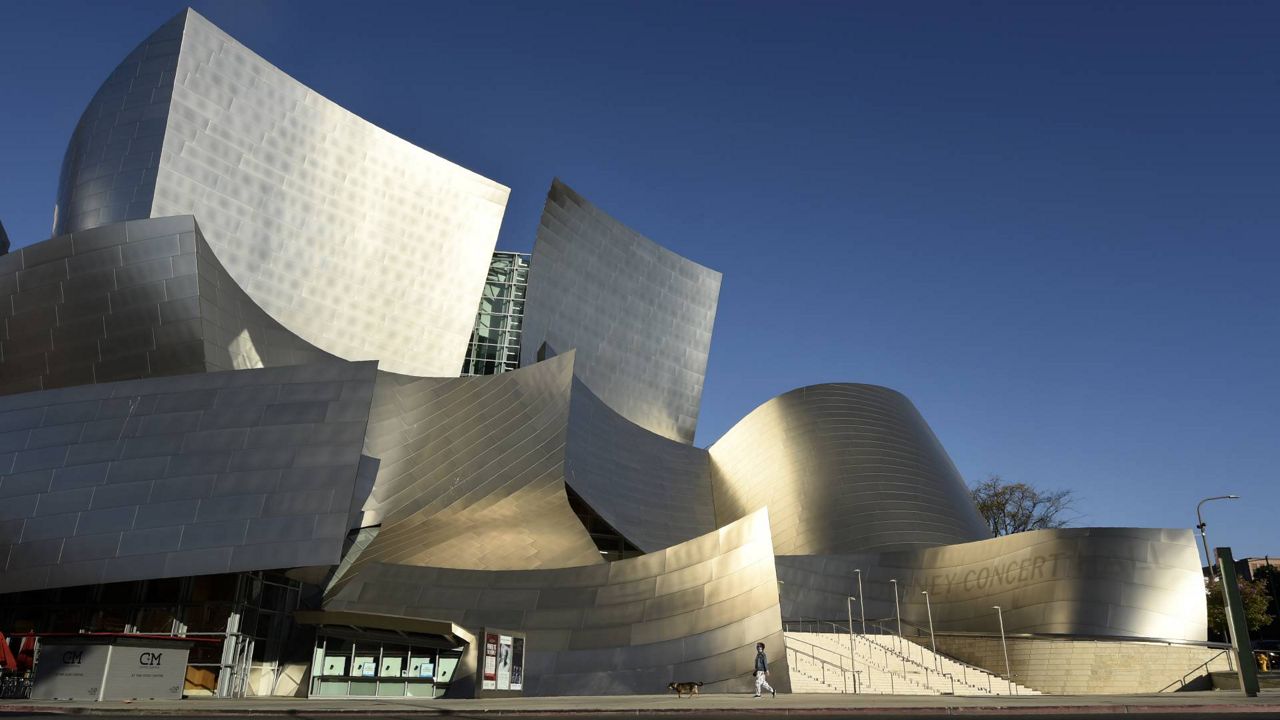 In this April 25, 2020 photo, a woman walks her dog past the Walt Disney Concert Hall on a deserted Grand Avenue, as stay-at-home orders continue in Los Angeles. (AP/Chris Pizzello)