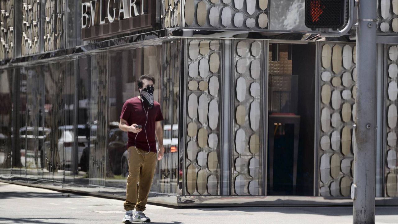 A man wearing a bandana waits for a traffic light on an empty Rodeo Boulevard in Beverly Hills during the coronavirus pandemic. (AP Photo/Richard Vogel)