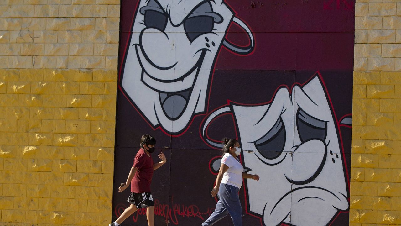 Pedestrians wear face masks as they walk past a street mural in Los Angeles on Thursday, May 14, 2020. (AP Photo/Damian Dovarganes)