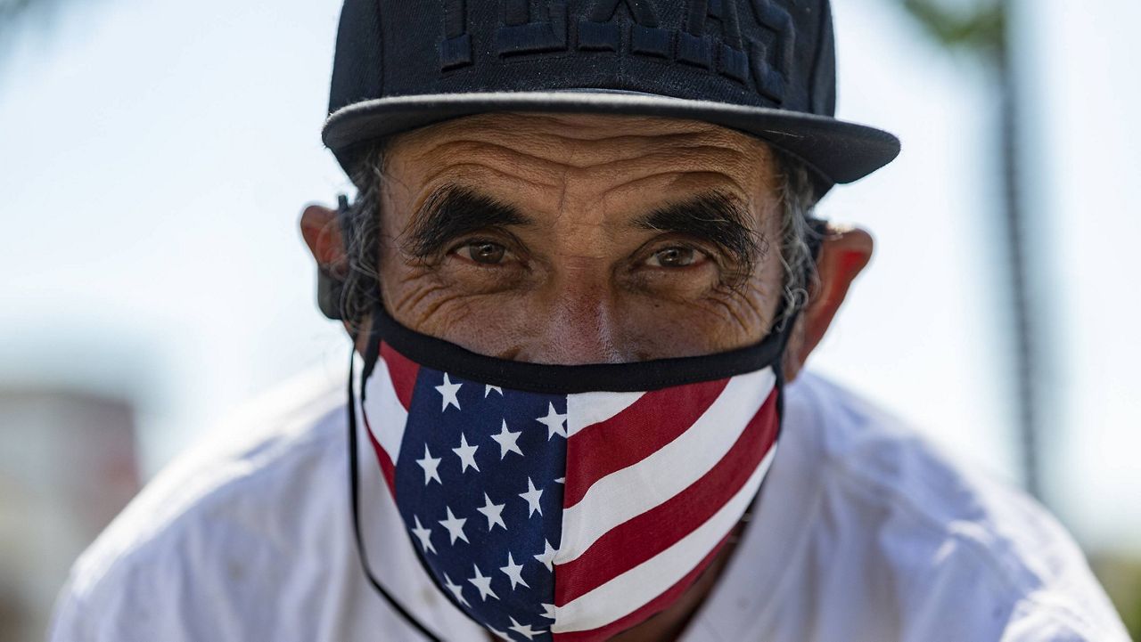 In this file photo from May 14, 2020, street seller Jaime Caldera, originally from San Antonio, Texas, offers face masks for sale in Los Angeles. (AP Photo/Damian Dovarganes)