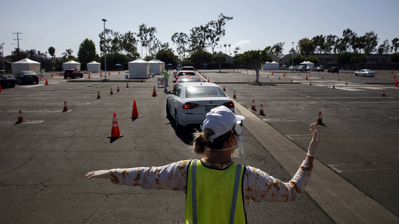 In this file photo from Friday, May 22, 2020, a volunteer controls traffic at a city-run, drive-thru COVID-19 testing site in South Central Los Angeles. (AP Photo/Jae C. Hong)