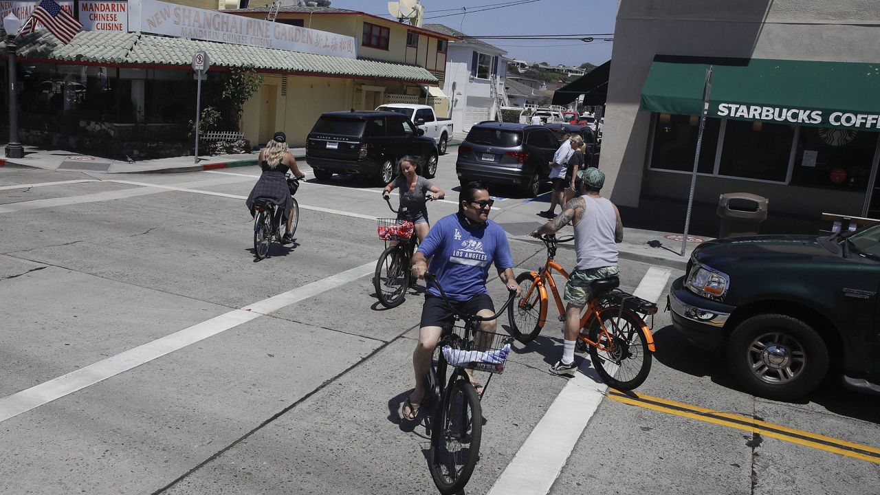 Bicyclists cross a busy street Sunday, May 24, 2020, on Balboa Island in Newport Beach, Calif. (AP Photo/Marcio Jose Sanchez)