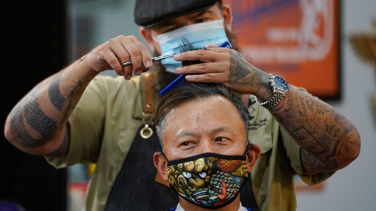 Luis Lopez wears a face mask while giving a hair cut to Alexander Chin at Orange County Barbers Parlor on Wednesday, May 27, 2020, in Huntington Beach, Calif. (AP Photo/Ashley Landis)