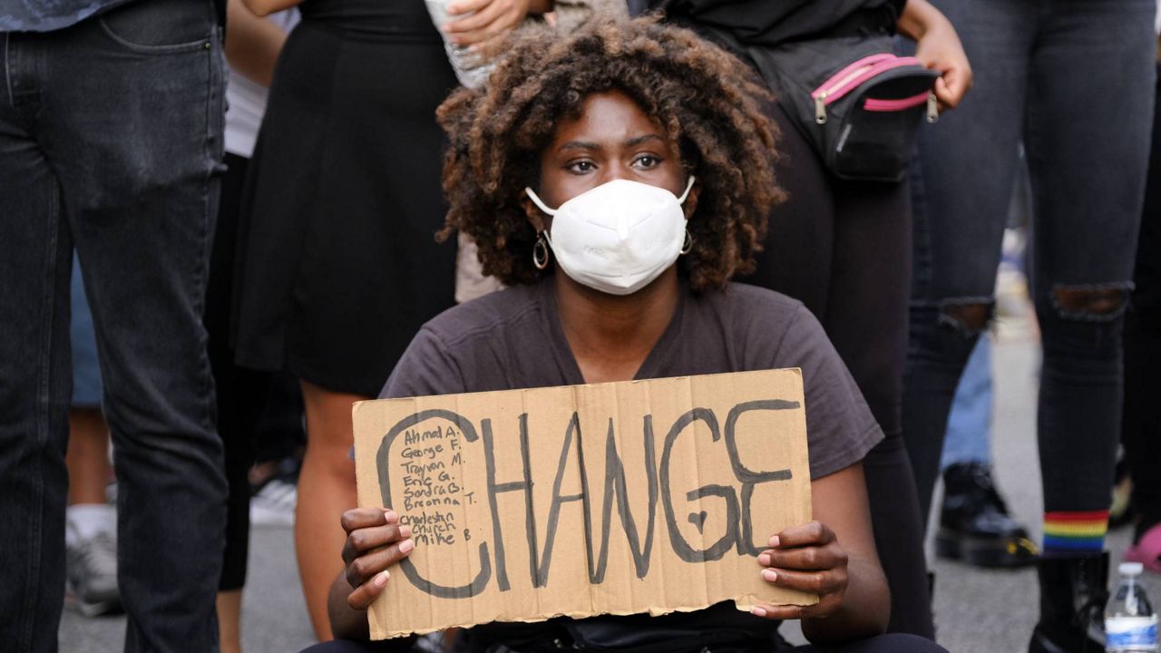 FILE - A Black Lives Matter protester sits and holds a sign for change outside Los Angeles Mayor Eric Garcetti's house on June 2, 2020. (AP/Richard Vogel)