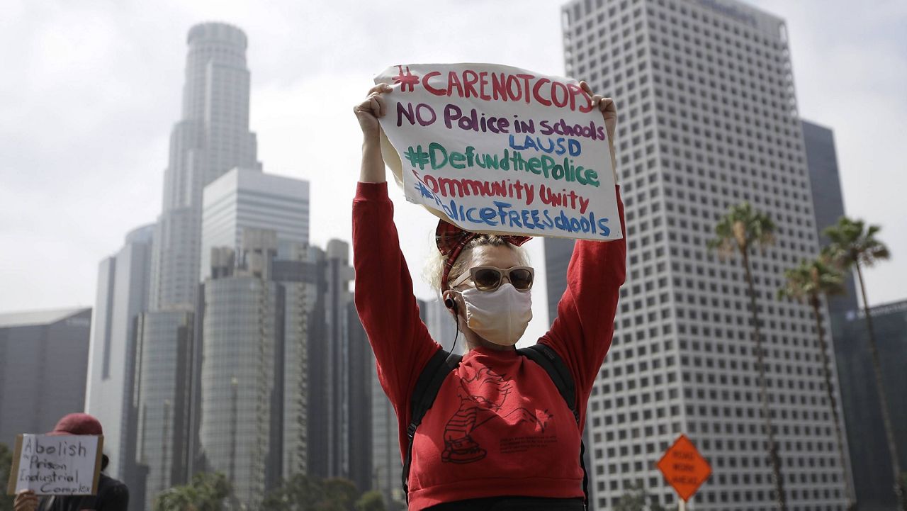 A demonstrator holds a sign in front of the downtown skyline during a protest to demand the defunding of the Los Angeles school district police outside of the school board headquarters Tuesday, June 23, 2020, in Los Angeles. (AP Photo/Marcio Jose Sanchez, File)