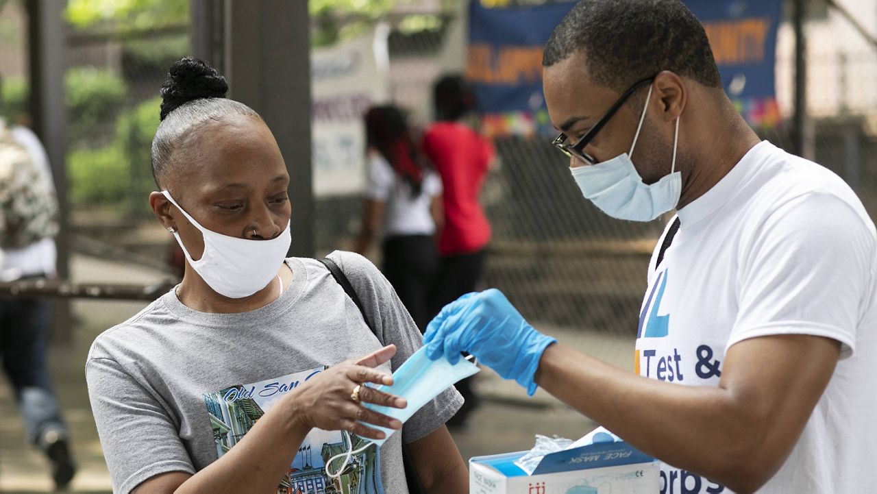 In this July 8, 2020, file photo, Stephane Labossiere, right, with the New York City Mayor's Office of Immigrant Affairs, hands out masks. (AP Photo/Mark Lennihan, File)