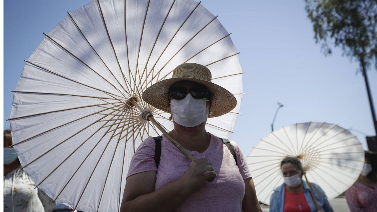 Churchgoers use face masks and parasols during an outdoor prayer amid the coronavirus pandemic at the San Gabriel Mission, Sunday, July 12, 2020. (AP Photo/Marcio Jose Sanchez)