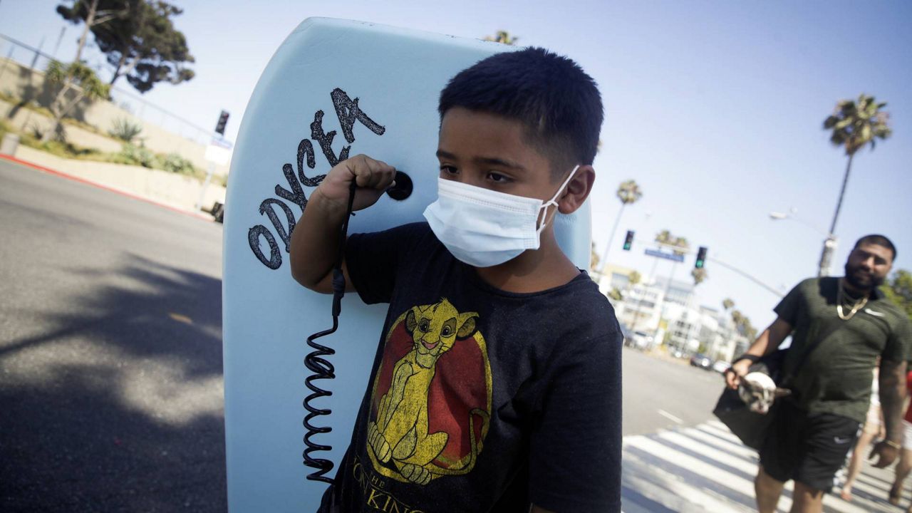 A boy wear a face mask as he carries a boogie board to the beach Sunday, July 12, 2020, in Santa Monica, Calif., amid the pandemic. (AP/Marcio Jose Sanchez)
