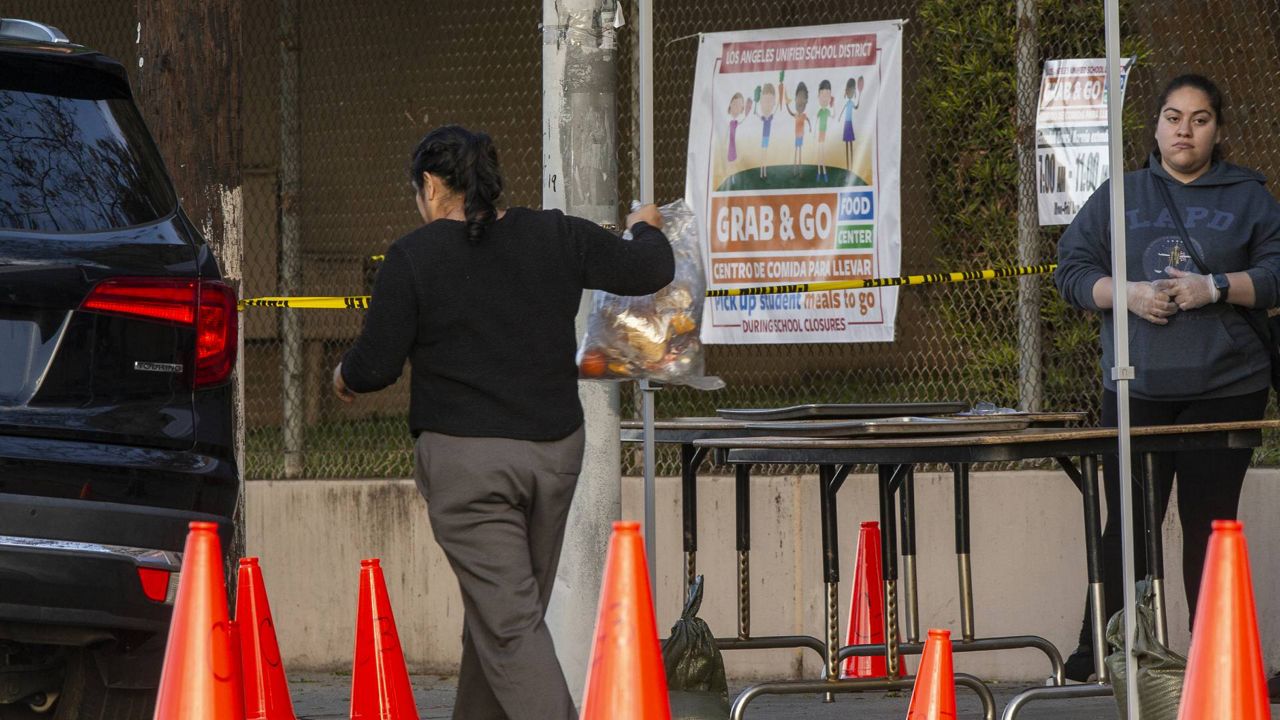 FILE - People step out of their vehicles at a "Grab & Go" stop to get free school meals provided by the Los Angeles Unified District at the Virgil Middle School station, March 25, 2020. (AP/Damian Dovarganes)