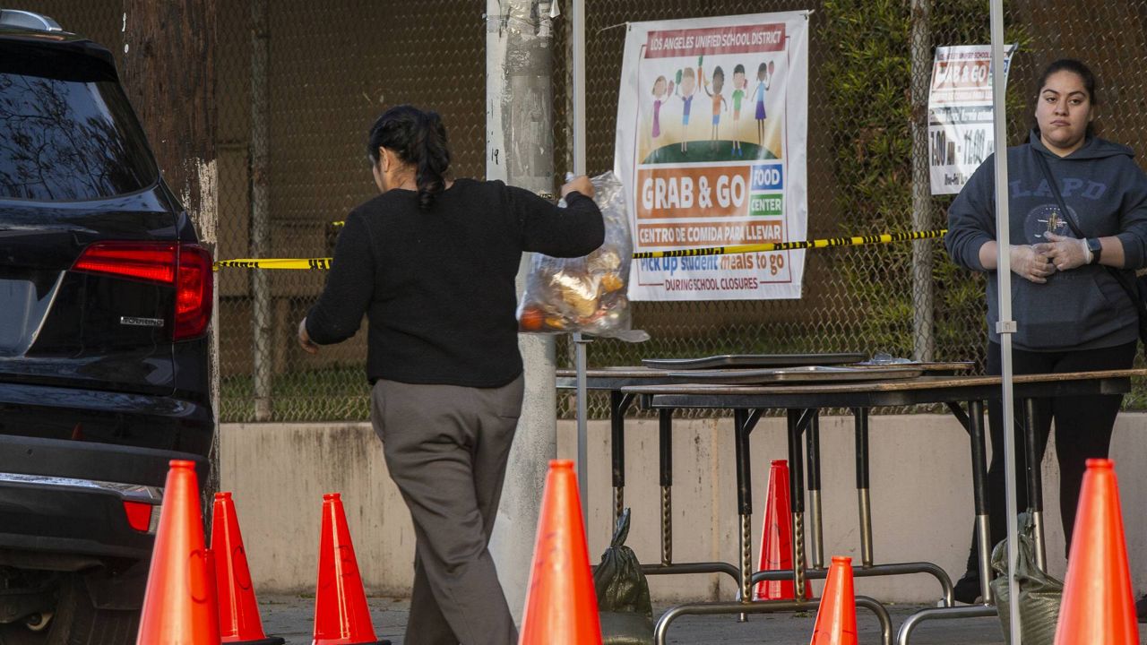 People step out of their vehicles at a "Grab & Go" stop to get free school meals provided by the Los Angeles Unified District at the Virgil Middle School station in L.A., March 25, 2020. (AP/Damian Dovarganes, File)