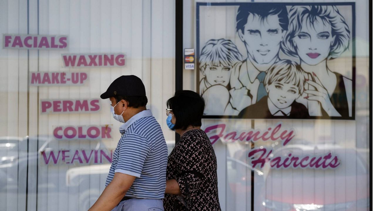 A couple wearing protective masks walk by a closed hair salon in L.A., July 14, 2020. Hair salons and barbershops will be allowed to reopen for limited indoor service, the county announced Wednesday. (AP Photo/Richard Vogel)