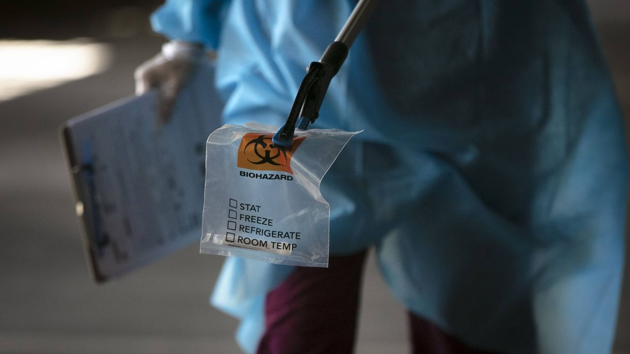 A physician assistant carries a nasal swab sample using a grabber at a COVID-19 drive-through testing site set up at the Anaheim Convention Center in Anaheim, Calif., Thursday, July 16, 2020. (AP Photo/Jae C. Hong)