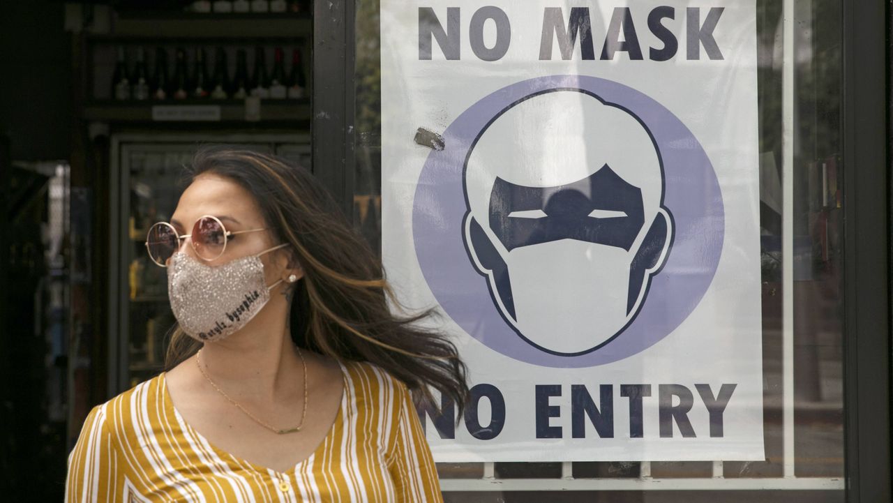 A woman walks out of a liquor store past a sign requesting its customers to wear a mask Tuesday, June 23, 2020, in Santa Monica, Calif. (AP Photo/Jae C. Hong, File)