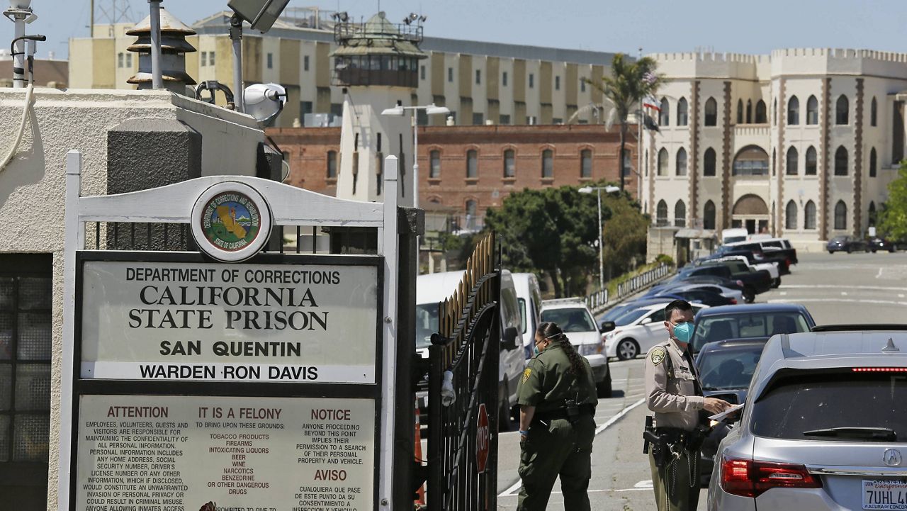 In this July 9, 2020, file photo, a correctional officer checks a car entering the main gate of San Quentin State Prison in San Quentin, Calif. (AP Photo/Eric Risberg, File)