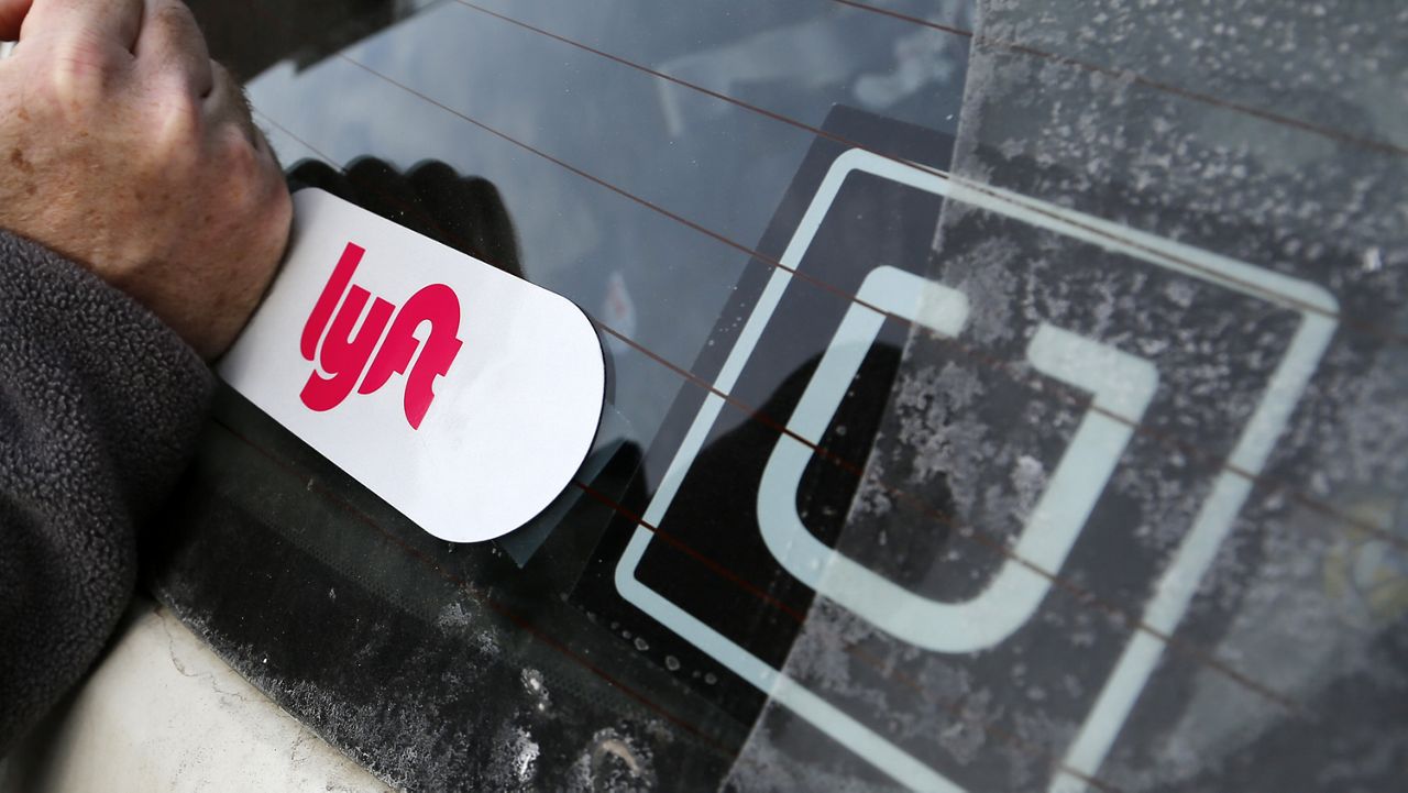 In this Jan. 31, 2018, file photo, a Lyft logo is installed on a Lyft driver's car next to an Uber sticker in Pittsburgh. Ride-hailing giants Uber and Lyft on Thursday, Aug. 20, 2020, are saying they will shut down their California operations if a new law goes into effect overnight which would force both companies to classify their drivers as employees. (AP Photo/Gene J. Puskar, File)