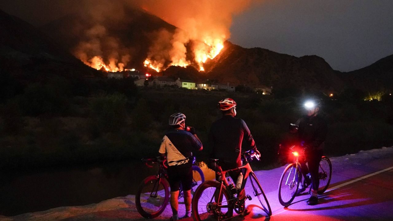 Cyclists rest along a trail as the Ranch Fire burns, Thursday, Aug. 13, 2020, in Azusa, Calif. Heat wave conditions were making difficult work for fire crews battling brush fires and wildfires across Southern California. (AP Photo/Marcio Jose Sanchez)