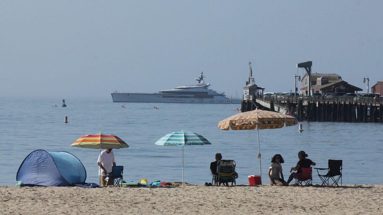 Early beachgoers secure spots on the shore at Santa Barbara, Calif., on Sunday, Aug. 16, 2020, as the superyacht Bravo Eugenia lies offshore. Californians packed beaches, lakes and recreation areas Sunday to seek relief from a record heat wave that strained the electricity grid and threatened to trigger a third round of rolling power outages. The heat wave brought triple-digit temperatures and raised wildfire danger and fears of coronavirus spread — a major concern in a state that has seen more than 621,000 confirmed cases. Public health officers urged people to follow mask and social distancing orders if they head outdoors. (AP Photo/John Antczak)