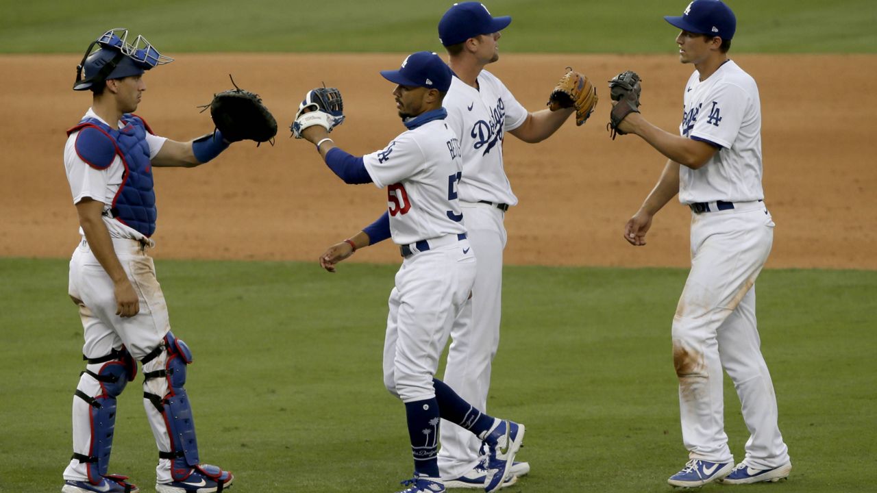 Los Angeles Dodgers catcher Austin Barnes, left, congratulates right fielder Mookie Betts, second from left, with shortstop Corey Seager, right, congratulating relief pitcher Blake Treinen, after the Dodgers defeat the Seattle Mariners, 2-1, in a baseball game in Los Angeles, Tuesday, Aug. 18, 2020. (AP Photo/Alex Gallardo)