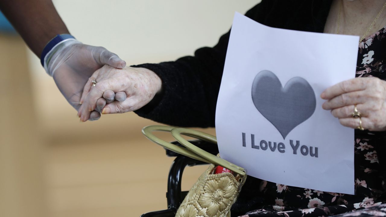 FILE - In this July 17, 2020 file photo, a senior citizen holds the hand of a care coordinator at a Health facility in Miami. (AP Photo/Wilfredo Lee)