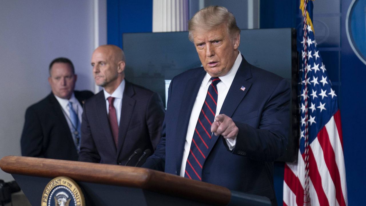 President Donald Trump speaks, accompanied by FDA Commissioner Dr. Stephen Hahn, center, during a media briefing at the White House, Sunday, August 23, 2020. (AP Photo/Alex Brandon)