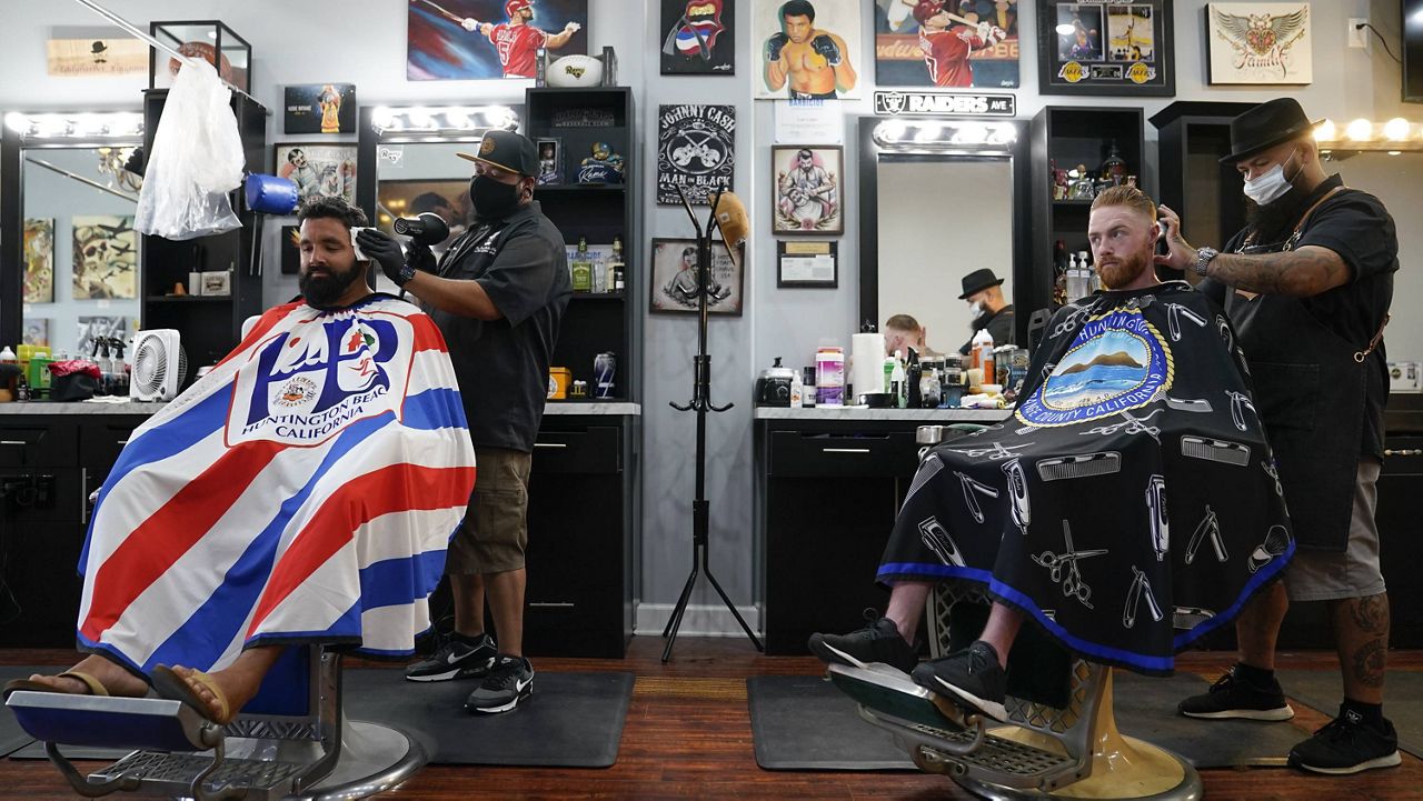 In this July 15, 2020, file photo, Ricardo Rivera, left, has his hair cut by Anthony Acosta while Braunson McDonald has his hair cut by Luis Lopez, right, owner of Orange County Barbers Parlor in Huntington Beach, Calif. (AP Photo/Ashley Landis)