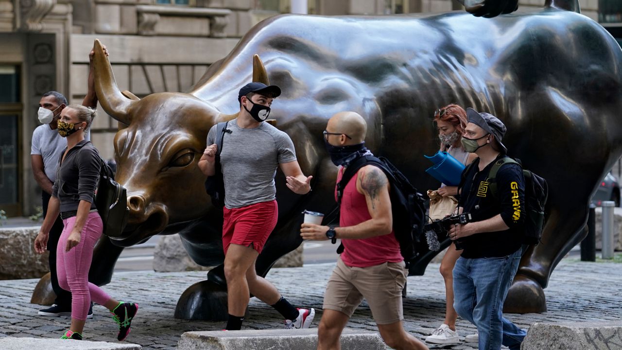 People wearing masks pass the Charging Bull statue in New York's financial district, Tuesday, Sept. 8, 2020. More sharp declines for big tech stocks are dragging Wall Street toward a third straight loss on Tuesday.