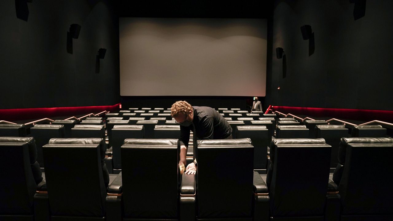 An employee cleans the seats in preparation for reopening at a Regal move theater in Irvine, Calif., Tuesday, Sept. 8, 2020.  (AP Photo/Jae C. Hong)