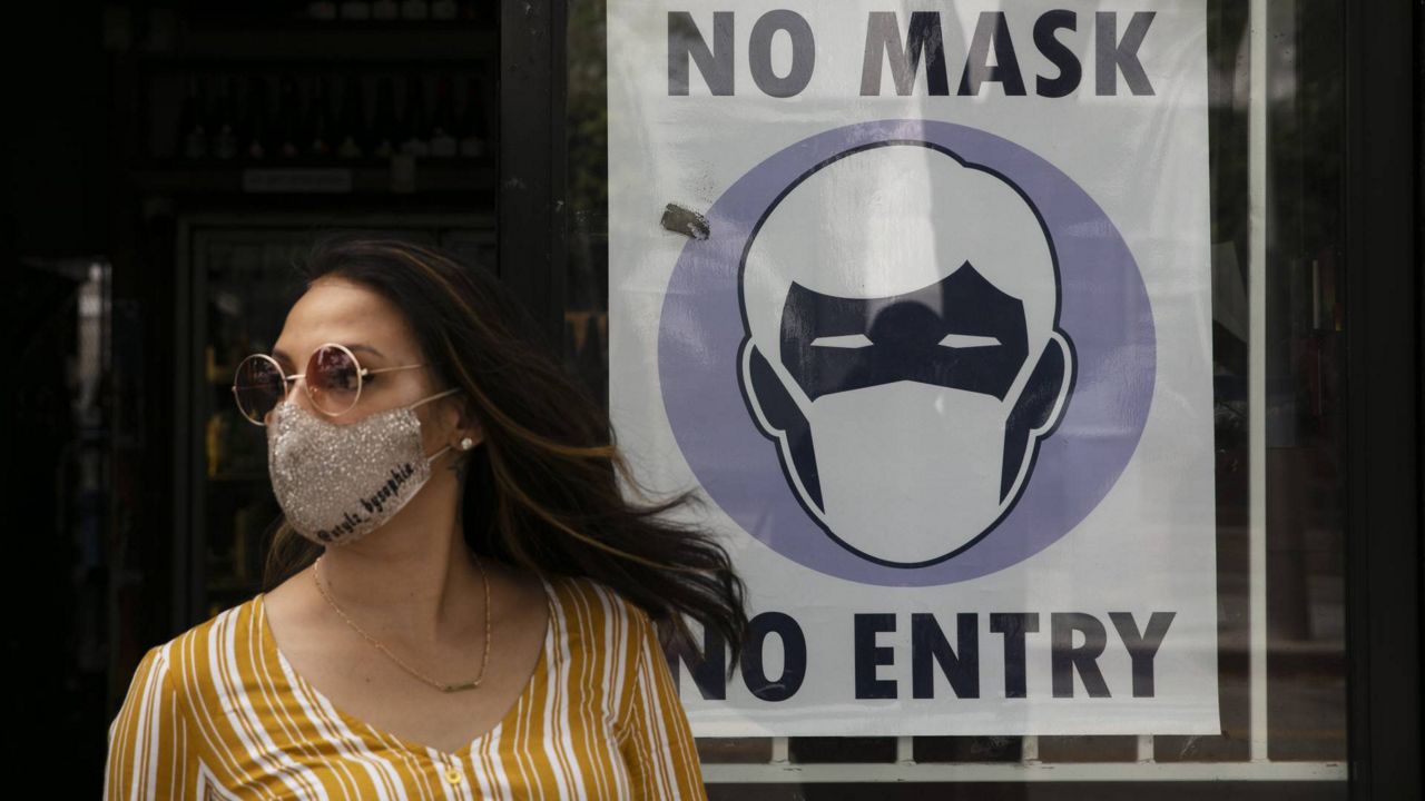 In this June 23, 2020 photo, a woman walks out of a liquor store past a sign requesting its customers to wear a mask in Santa Monica, Calif. (AP Photo/Jae C. Hong, File)